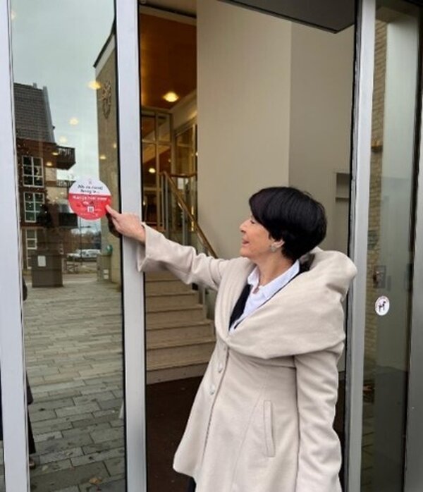 Wethouder Willy Hendriks-van Haren plakt de eerste sticker op de ingang van het gemeentehuis in Cuijk